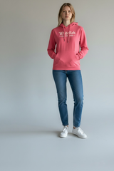 Person wearing a pink hoodie with text, blue jeans, and white sneakers on a plain background